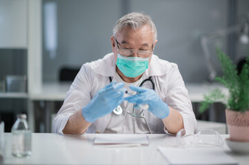 A serious, gray-haired doctor fills a syringe with a vaccine from a glass ampoule to vaccinate his patient against the coronavirus.