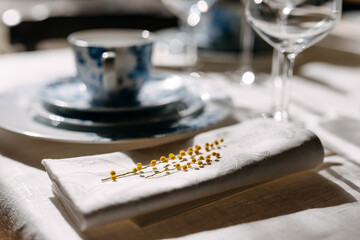 Closeup of mimosa twigs on napkin next to a vintage Chinese porcelain tableware.