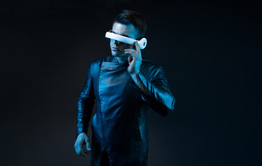 Young man in futuristic costume on dark background. Guy using VR helmet. Augmented reality, virtual...