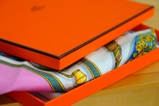 PARIS, FRANCE -27 FEB 2021- View of the Hermes logo name on a colorful Hermes silk scarf and a signature orange box. Hermes is a French leather and clothing brand.