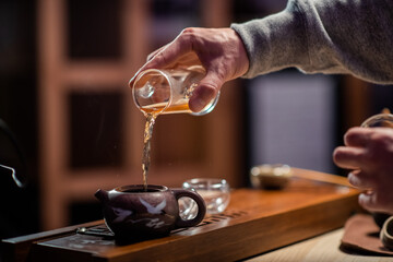Close-up of a traditional oriental tea ritual. A man pours black ripe tea from a flask into a tasting cup. Blurry background