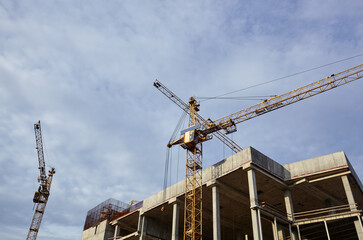Fototapeta na wymiar Tower cranes building a house. Concrete building under construction