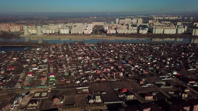 aerial view - a flight across the Kuban River from Alygeya with low-rise buildings to the microdistrict of the city of Krasnodar with multi-storey buildings and wide boulevards on a sunny day