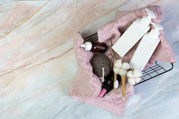Obraz na płótnie Canvas set of shower accessories in a basket on a marble background. contains bottles of cosmetics, loofah, toothbrushes, towel. DIY eco cosmetics. concept zero waste, sustainable. copy space. flat lay