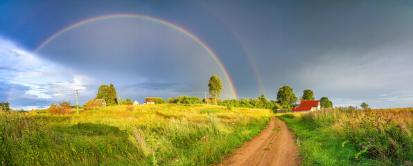 Rainbow over stormy sky. Rural landscape with rainbow over dark stormy sky in a countryside at...