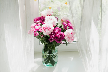 View of a bouquet of pink peonies and chrysanthemums in a vase on the window. Concept background, flowers, holiday.