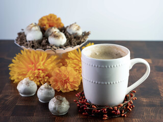 Cappuccino cake balls, coffee flavored truffle like dessert, decorated with fall orange flowers on a wooden table with white ceramic coffee mug and bowls.