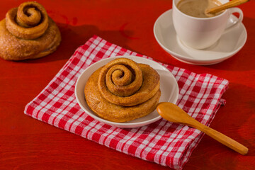 Freshly baked cinnamon bun stuffed with spices and cocoa on a red table with a tough shade. Sweet homemade cakes.