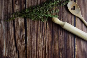 On rustic wooden table, kitchen utensils with stems of aromatic plant, rosemary. Copy space.