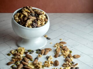 Raised dish filled with trail mix spilling out onto the herringbone counter.  Nuts, almonds, seeds, pumpkin, banana, raisin, walnut, cashew, pecan, granola, peanut, good healthy carbs and fat.