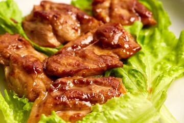 Caramelized chicken close-up top view. Asian recipe for caramelized chicken fillet slices on a plate in lettuce leaves on a wooden table