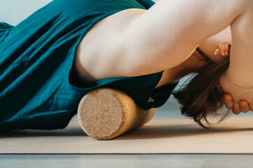 Partial body details of woman rolling back on a cork massage roller to release tension in back...