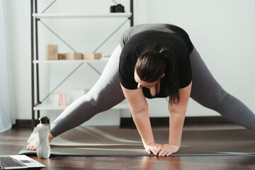 Fototapeta premium Home fitness, training online. Overweight woman looking tutorial video doing stretching exercise. Indoor yoga for home