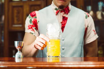 Bartender showing cocktail in a tiki glass on a bar counter on a blurred background of bottles in a
