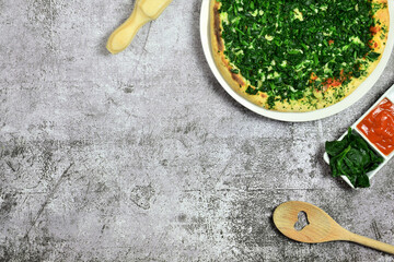 On gray stone, spinach pizza, cooking utensils and ingredients. Zenith view. Copy space. 