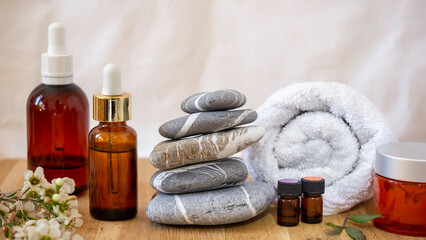 Dark glass vessel ,  essential oil cosmetic for skin care, massage and spa at home. Stack of stones, towel and white flowers on a wooden table. 