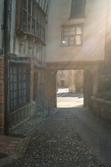 Harsh sunlight streaming in to a medieval courtyard of crooked Tudor style buildings in the city of Norwich