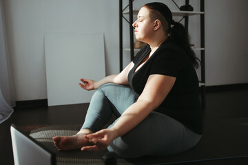 Home yoga, tranquility, harmony concept. Overweight woman meditating in her living room, yoga beginner