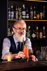 Elderly bartender gives red cocktail. Fresh cocktail alcoholic, non-alcoholic drink-beverage at the bar counter in the night club