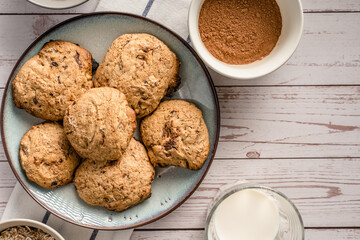 Close up top view on crunchy oatmeal chip cookies fresh baked biscuits with chocolate and cocoa in a plate on the table and ingredients beside homemade food concept