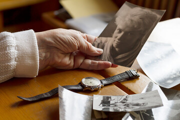 An old watch next to an old woman's hand. Next to old photos. Memories, nostalgia, time concept