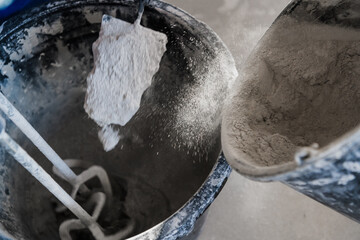 The builder puts dry plaster into the bucket. He uses a trowel