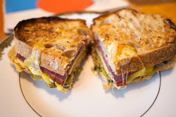 Toasted salt beef cut sandwich with melted cheese and pickle on a white plate.