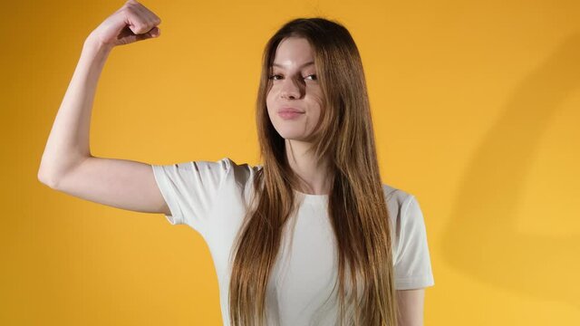 Young cute sporty smiling brunette woman showing arms and biceps on orange background.