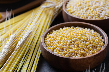 Raw couscous in bowl on wooden background with wheats, uncooked food concept