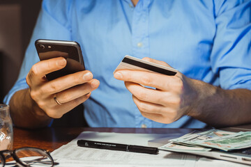 Stressed young businessman calculating monthly Family expenses, taxes, checking bank account balance credit card payment, Income at home night. Cropped shot male hands paying bill online on smartphone