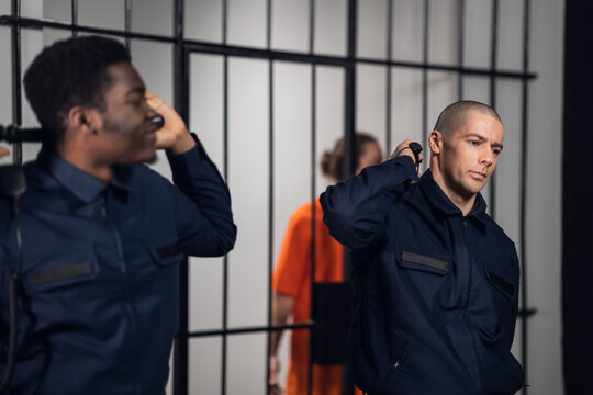 Black and white prison guards stand with batons in the background of cells with prisoners criminals