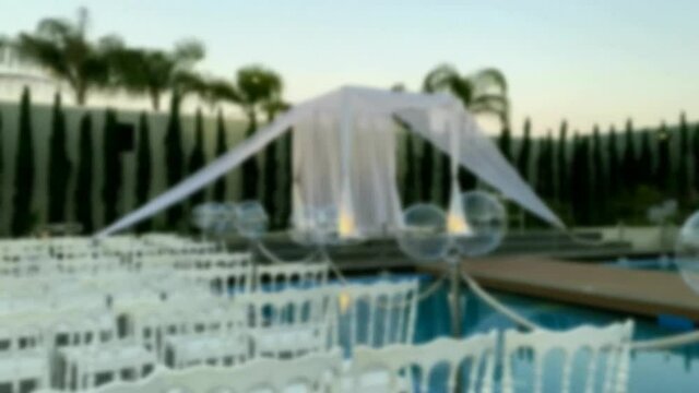 Jewish traditions wedding outdoor ceremony. Wedding canopy (chuppah, hupa)  against the background of evening sky, palms and an artificial reservoir decorated with balloons. Blurred view. HD