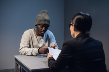 A lawyer girl with glasses and a young black guy communicate in the interrogation room about the grounds for his detention.