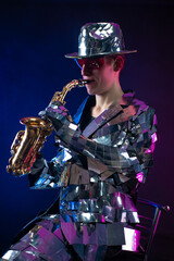 Fototapeta na wymiar a male artist in a mirrored suit and a hat with a saxophone in neon light