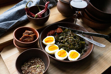 Boiled eggs, seaweed, sun-dried tomatoes sprinkled with pumpkin seeds, flax seeds and seeds in a clay plate and a glass of wine on a light wooden surface