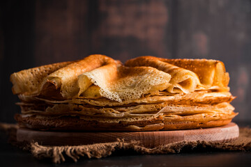 Traditional Russian food - thin pancakes. A stack of crepes on a dark brown wooden background. Rustic style.