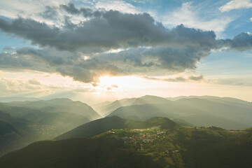 A village in Rhodope Mountains lit by sunrays, under dramatic sky, Bulgaria