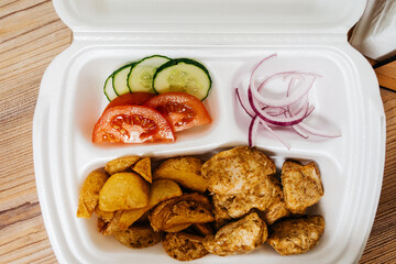 Meat, french fries and vegetables platter in plastic container