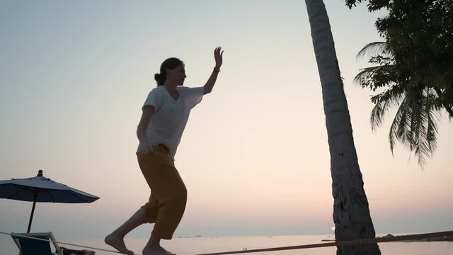 The girl goes on a slackline at sunset on a tropical beach. 