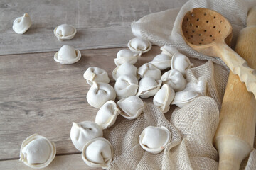 Homemade raw dumplings with flour on a wooden white background.