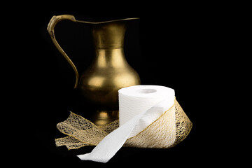 a roll of toilet paper and a brass water pitcher with a golden ribbon isolated on black
