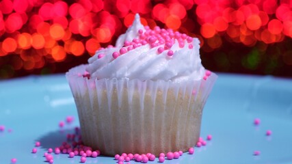 Cupcake macro shallow depth of field and decoration with sugar sprinkles. Cup cake with white vanilla cream on red background. Process of making delicious desserts muffin for birthday or Valentine.