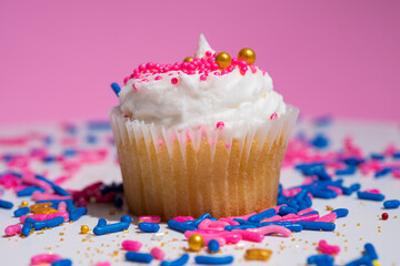 Cupcake macro shallow depth of field view. Decorated sugar sprinkles cup cake with white vanilla cream on pink background. Delicious desserts muffin for girl birthday or Valentine day.