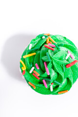 Green frosted vanilla cupcake with rainbow sprinkles on a white background