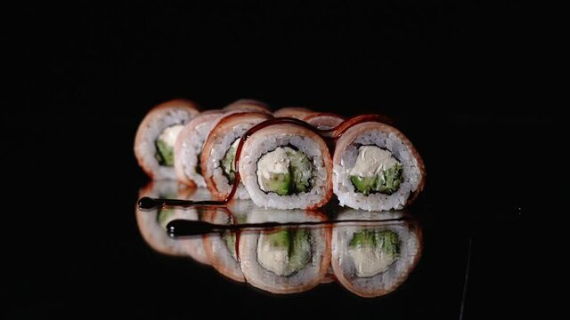 Chef's hands sprinkle sesame seeds on the inside out sushi. Japanese chef in black gloves at work preparing sushi roll with salmon and avocado.