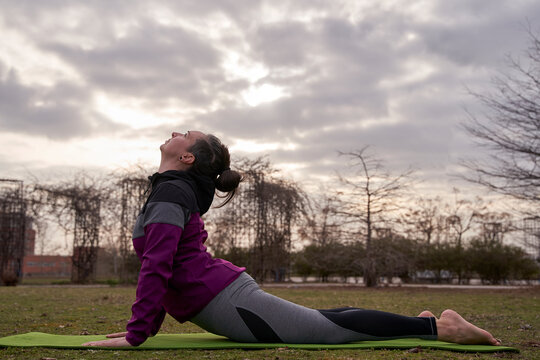  Young woman practicing Bhujangasana or Cobra Pose in a park.