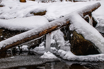Icy wood log and rocks covered in snow in winter freezing river