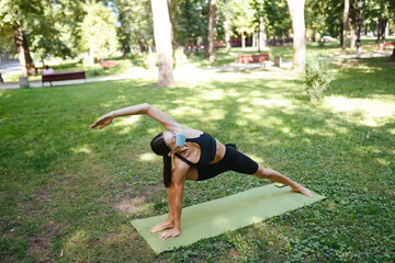 Athletic young woman in a medical protective mask, doing yoga in the Park