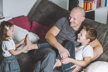 Father laughs and plays with his children. Man with his son and daughter having fun at home.