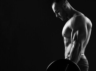 Silhouette of Brutal strong man athlete in jeans lifting bar showing pumped up sexy body and biceps over dark background, side view, copy space. Sport men body concept